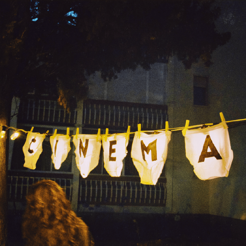 cinema-no-estendal Weiße riesige Unterhosen an einer Wäscheleine mit Buchstaben, die das Wort 'CINEMA' bilden, bei Nacht.